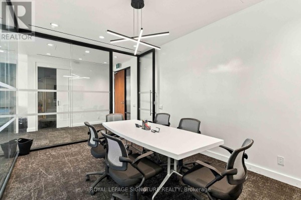 Conference room with a white table, chairs, and white walls, looking out through glass walls to an office. - 1005 - 130 Queens Quay E, Toronto