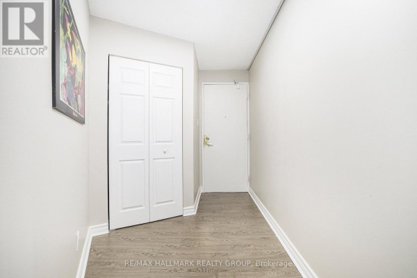 Apartment hallway with light grey walls, a closet with bi-fold doors, and a white door. - 1005 - 1380 Prince Of Wales Drive, Ottawa