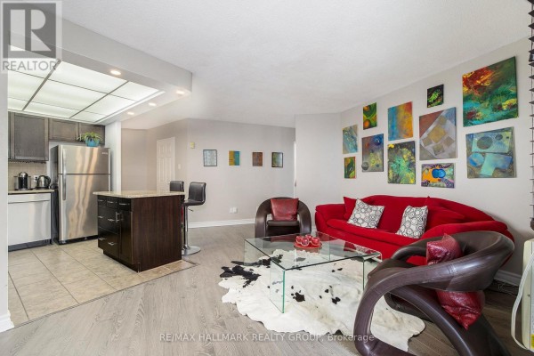 Living room and kitchen with a red sofa, glass coffee table, and island with bar stools. - 1005 - 1380 Prince Of Wales Drive, Ottawa