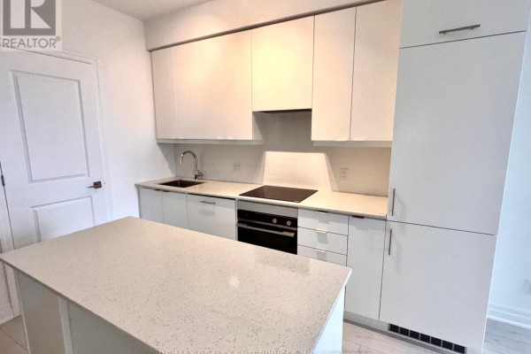 Modern white kitchen with a quartz island, stainless steel appliances, and white cabinetry. - 1005 - 30 Elm Drive W, Mississauga