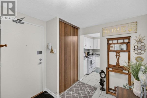 Entryway with a large white door, wooden closet, hallway leading to a white kitchen. - 1005 - 415 Greenview Avenue, Ottawa