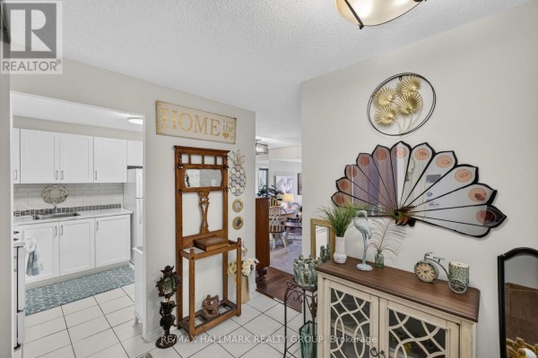 Hallway showing a wooden hall tree, cabinets, mirrored wall decor, and view into kitchen and dining area. - 1005 - 415 Greenview Avenue, Ottawa