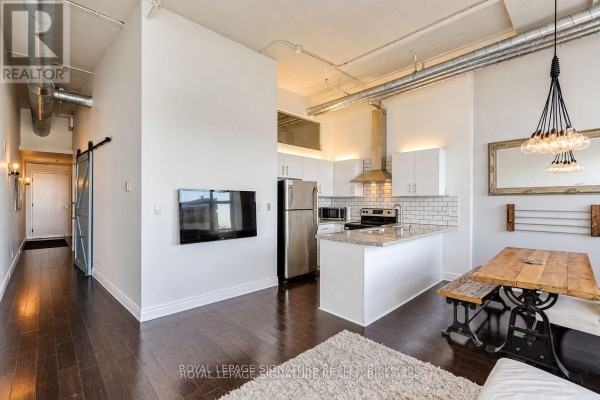Hallway leading to a sliding barn door, with a kitchen and dining area visible. - 1005 - 700 King Street W, Toronto