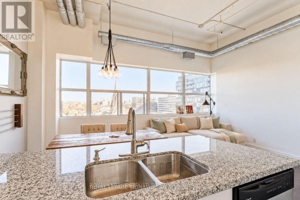 View from the kitchen island showing the dining area and living room with a large window. - 1005 - 700 King Street W, Toronto