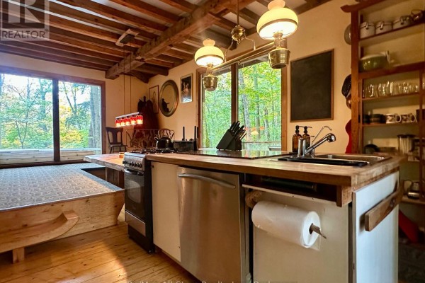 View of a kitchen with wooden beams, exposed shelving, and large windows overlooking the trees and lake. - 1005 Mcarthur Point Road, Lake Of Bays