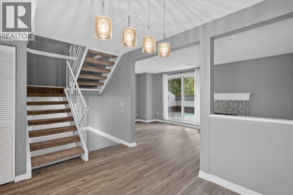 Townhouse interior with light grey walls, a staircase with white railing, and sliding glass doors. - 1006, 2520 Palliser Drive Sw, Calgary
