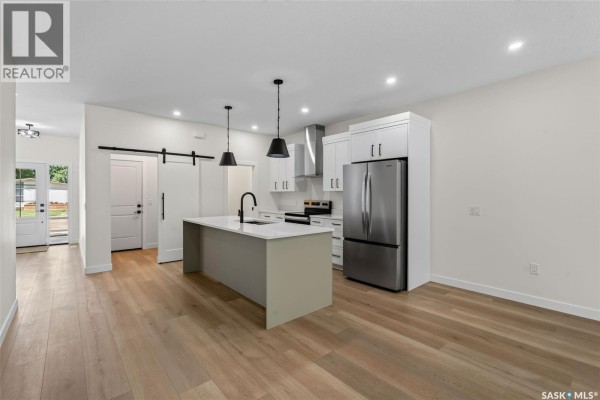 Open-concept kitchen with white cabinets, island, stainless steel appliances, and wood flooring. - 1006 10th Street, Humboldt