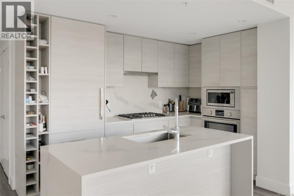 Kitchen with light wood cabinets, white quartz island, stainless steel appliances, and wine rack. - 1006 777 Herald St, Victoria