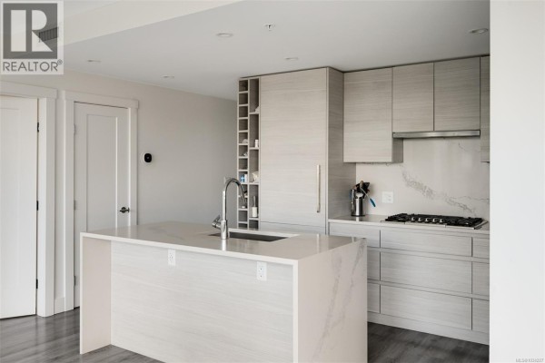 Kitchen with light wood cabinetry, quartz countertops, and an island with a sink and faucet. - 1006 777 Herald St, Victoria