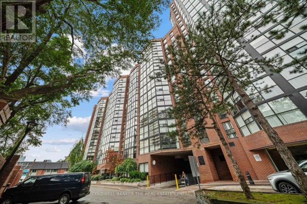 Exterior view of a tall brick and glass apartment building with trees in the foreground. - 1007 - 701 King Street W, Toronto