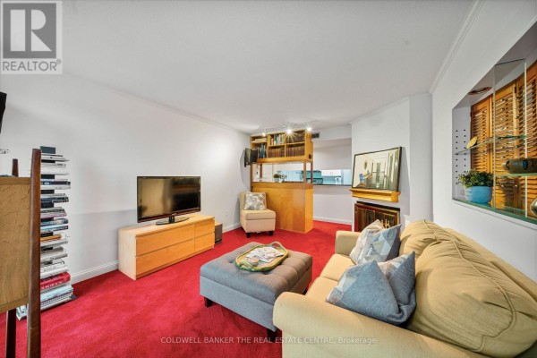 Living room with red carpet, beige sofa, armchair, television, and a wooden bar area. - 1007 - 701 King Street W, Toronto