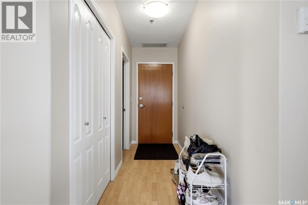 Apartment hallway with a wooden front door, mirrored closet doors, and shoe rack. - 1007 1914 Hamilton Street, Regina