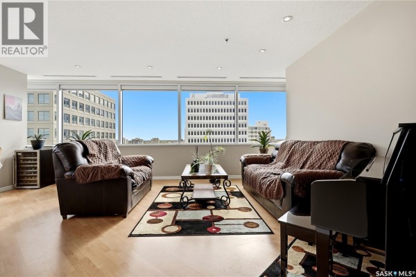 Living room with two brown leather sofas, coffee table, rug, and large windows. - 1007 1914 Hamilton Street, Regina