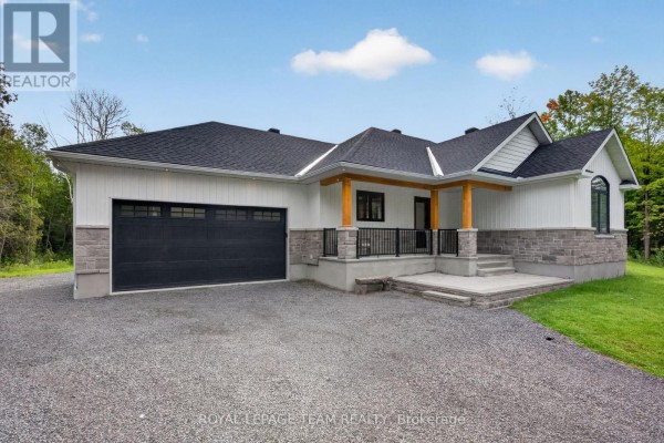 Side view of a white and stone bungalow with a black garage door and front entrance. - 1007 Townline Road, North Grenville