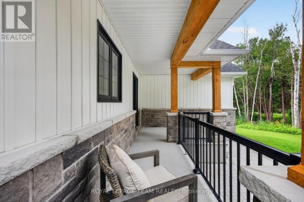 Covered front porch with wooden beams, stone base, and black railing on a white house. - 1007 Townline Road, North Grenville