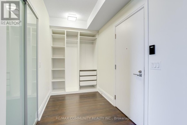 Walk-in closet with white built-in shelves, drawers, and dark wood flooring. - 1008 - 120 Harrison Garden Boulevard, Toronto