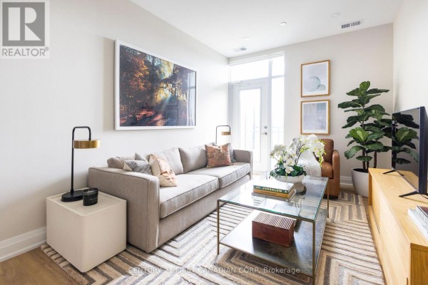 Living room with a grey sofa, glass coffee table, and large abstract wall art. - 1008 - 4286 King Street, Kitchener