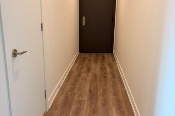 Interior hallway with light wood laminate flooring, white walls, and a dark brown door. - 1008 - 91 John Street, Hamilton