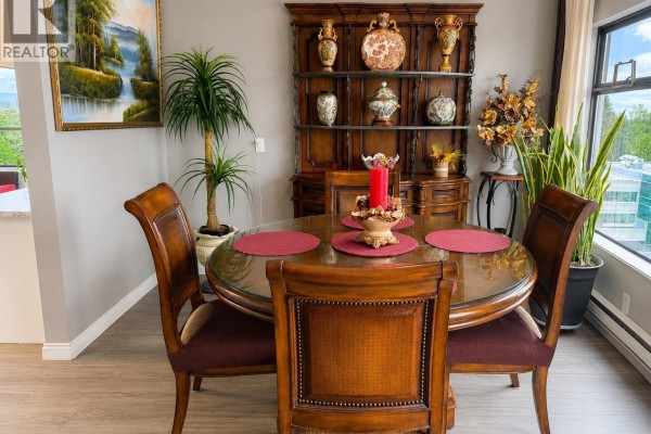 Close-up of a round glass dining table with four wooden chairs, a decorative hutch, and plants. - 1008 615 Belmont Street, New Westminster