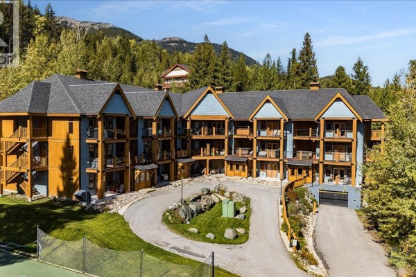 Aerial view of a large apartment building complex surrounded by trees and mountains. - 1008 Olaus Way Unit# 2, Rossland