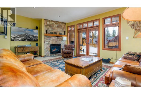 Living room with leather couches, stone fireplace, large rug, and wood trim. - 1008 Olaus Way Unit# 2, Rossland