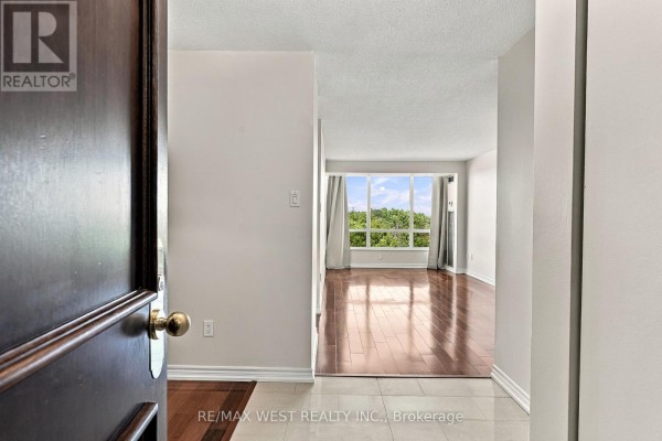 View from the entrance of an apartment showing a living area with hardwood floors and a large window. - 1009 - 1320 Islington Avenue, Toronto