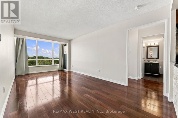 Apartment living room with dark hardwood floors, white walls, and a large window overlooking trees. - 1009 - 1320 Islington Avenue, Toronto