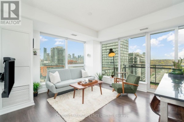 Living room with grey sofa, green armchair, coffee table, and large windows. - 1009 - 225 Sackville Street, Toronto
