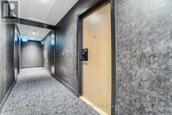 Hallway with dark patterned wallpaper, grey carpeting, and unit 1009 door visible. - 1009 - 2300 St. Clair Avenue W, Toronto