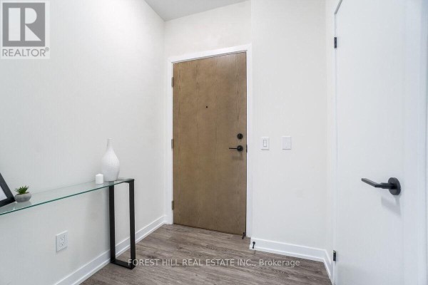 Interior entryway with a light wood door, white walls, and a narrow glass console table. - 1009 - 2300 St. Clair Avenue W, Toronto