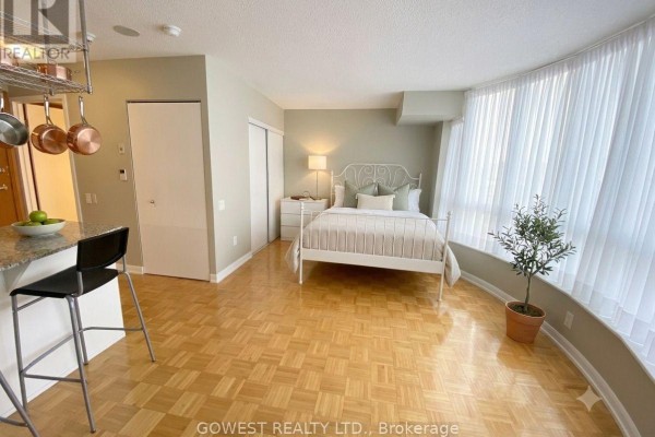 Studio bedroom with a white metal bed, hardwood floors, and large window. - 1009 - 33 Sheppard Avenue E, Toronto