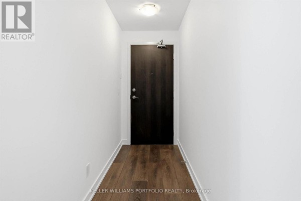 Long hallway leading to kitchen area, with doors on either side and hardwood flooring - 1009 - 50 Bruyeres Mews, Toronto