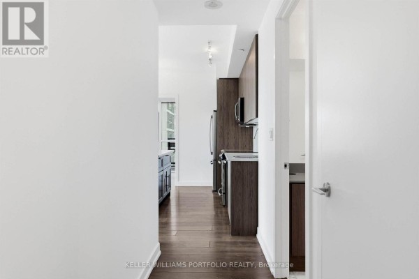 Open-concept living area with large windows, city view, and kitchen island with dark cabinetry - 1009 - 50 Bruyeres Mews, Toronto