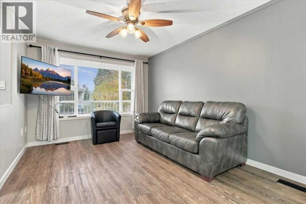 Living room with a grey leather couch, black armchair, and a television mounted on the wall. - 101, 10550 111 Street N, Grande Prairie