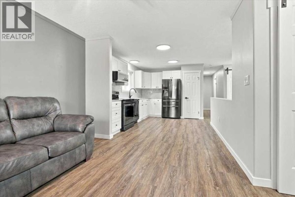Open concept living room and kitchen area with white cabinets and stainless steel appliances. - 101, 10550 111 Street N, Grande Prairie