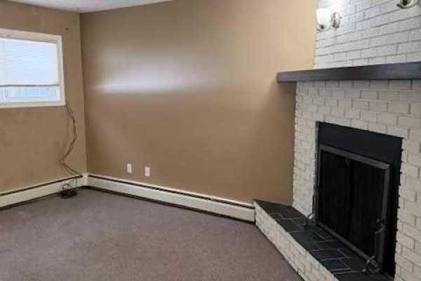Bedroom with tan walls, a window with white patterned curtains, and brown carpeted flooring. - 101, 11114 Hoppe, Grande Cache