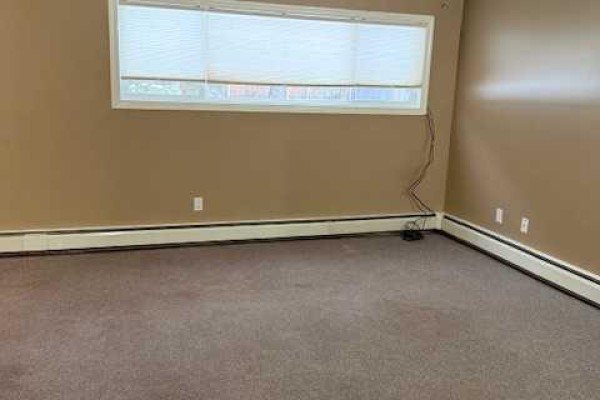 Hallway with tan walls, doors on both sides, and a view of a room with a window at the end. - 101, 11114 Hoppe, Grande Cache