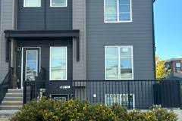 Exterior of a modern grey townhouse with dark trim and a covered front entrance. - 101, 260 Rowley Way Nw, Calgary
