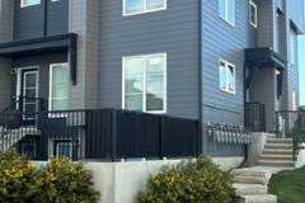 Exterior of a modern grey townhouse with dark trim and a covered front entrance. - 101, 260 Rowley Way Nw, Calgary