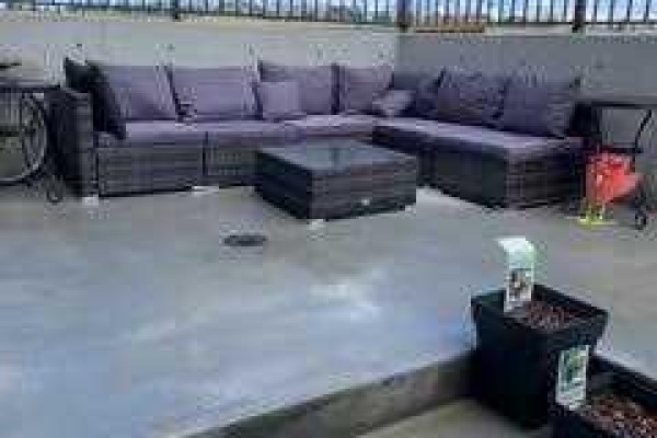 Rooftop patio with a grey sectional sofa, a dark wicker coffee table, and potted plants. - 101, 260 Rowley Way Nw, Calgary