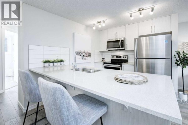 Bright open-concept kitchen with a white quartz island, stainless steel appliances, and light wood floors. - 101, 260 Rowley Way Nw, Calgary