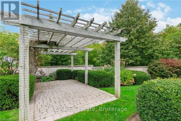 Paved patio area under a weathered wooden pergola with surrounding manicured bushes and lawn. - 101 - 10 Bay Street, Blue Mountains