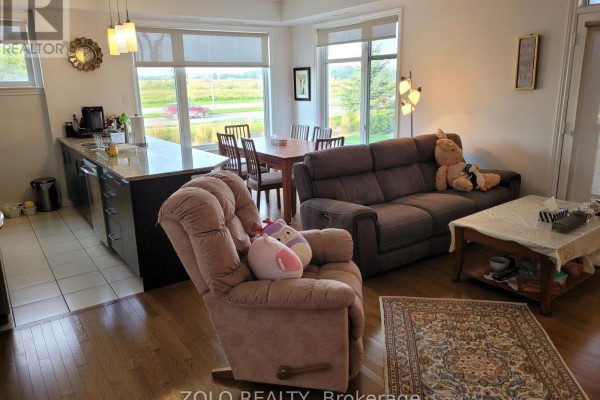 Living room with gray sofa and plush armchair, dining table, and kitchen island. - 101 - 130 Guelph Private, Ottawa