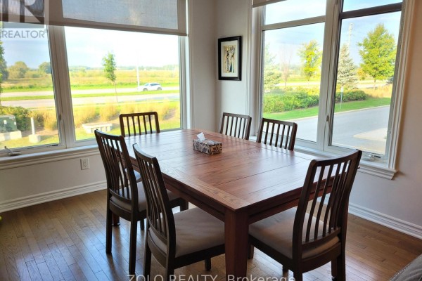 Dining area with wooden table and chairs, surrounded by large windows with greenery view. - 101 - 130 Guelph Private, Ottawa