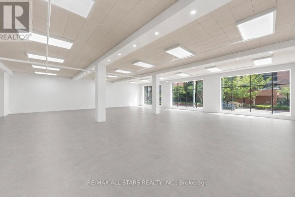 Empty commercial space with beige tiled floor, white walls, ceiling lights, and large windows. - 101 - 14 Mccaul Street, Toronto