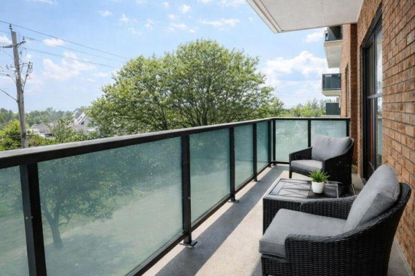 Balcony with glass railings overlooking green trees and a brick building exterior. - 101 - 1780 Lawrence Avenue E, Toronto