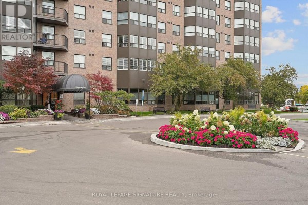 Entrance to the apartment building with a circular driveway, landscaping, and a covered entryway. - 101 - 2 Raymerville Drive, Markham