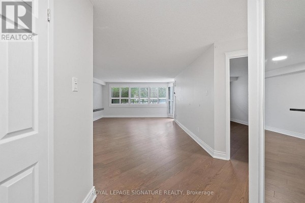 Interior view of an empty living room with light grey walls and dark hardwood floors. - 101 - 2 Raymerville Drive, Markham