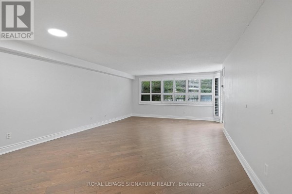 Interior view of a spacious living room with white walls and large windows with blinds. - 101 - 2 Raymerville Drive, Markham