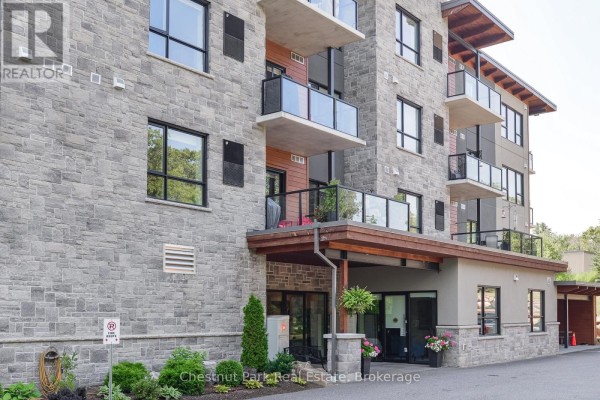 Close-up of the apartment building entrance with stone facade, glass balconies, and covered walkway. - 101 - 23 Campus Trail, Huntsville
